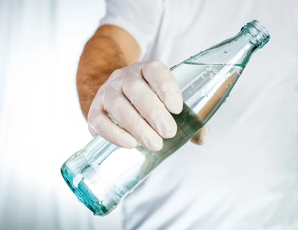 Manlig hand i latex handske hålla glasflaska vatten — Stockfoto