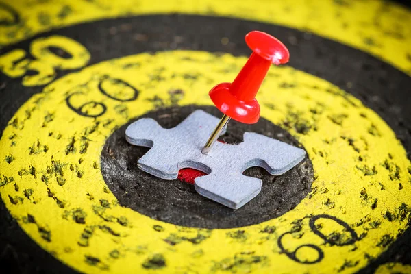 Red pin stuck to man shape jigsaw puzzle piece on old target board