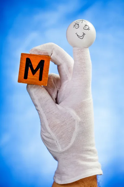 Finger puppet holding wooden cube with capital letter M