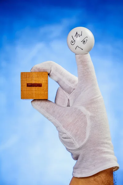 Finger puppet holding wooden cube with minus sign — Stock Photo, Image