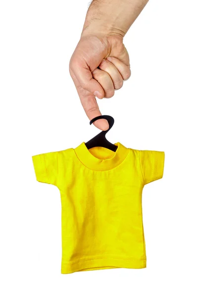 Mano masculina sosteniendo en el dedo pequeña camiseta amarilla en gancho negro —  Fotos de Stock