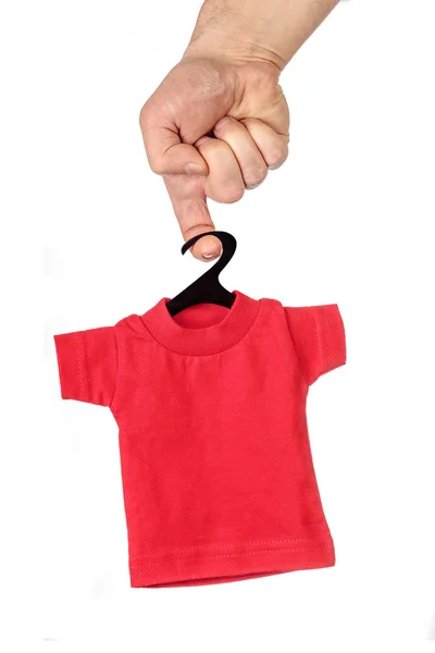 Männliche Hand hält am Finger kleines rotes T-Shirt auf schwarzem Bügel — Stockfoto