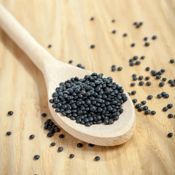 Black lentils on wooden spoon — Stock Photo, Image