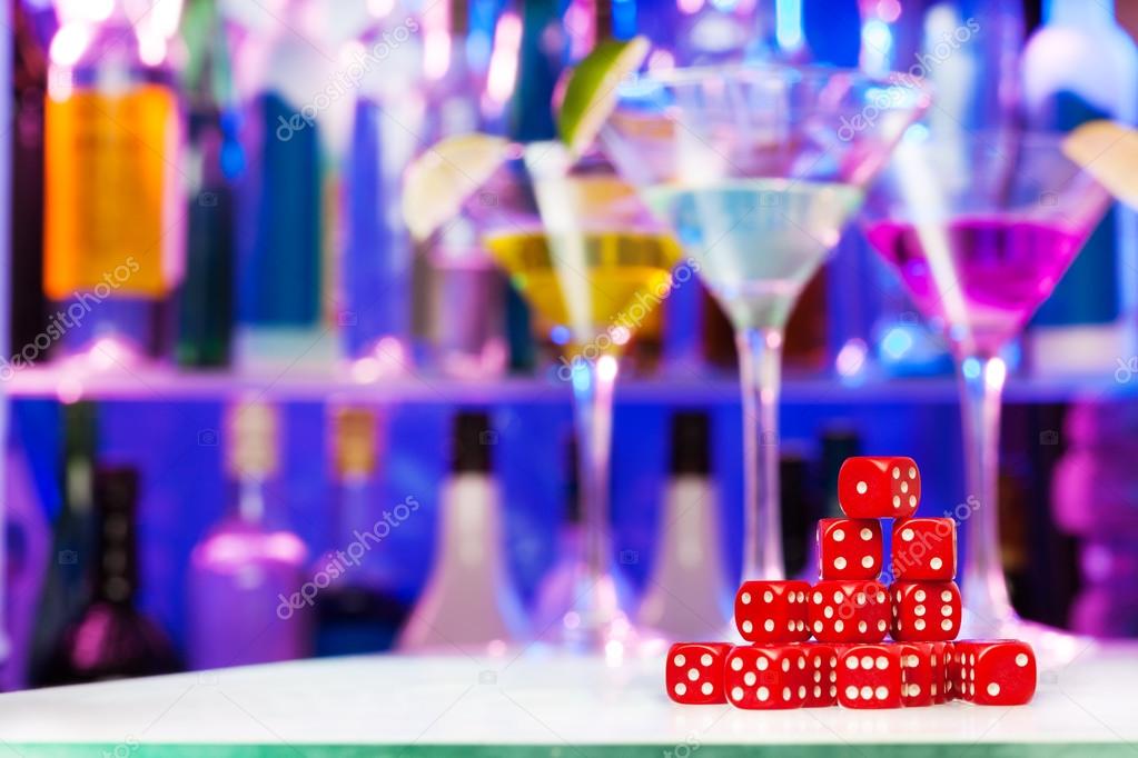 Heap of red playing dices, bar bottles and glasses