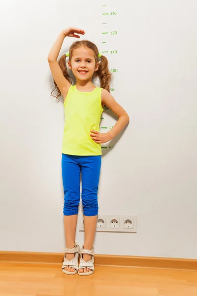 Cute girl checking height on wall with hand — Stock Photo, Image