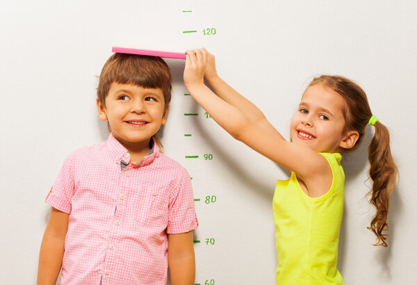 Boy and girl measure height by wall scale