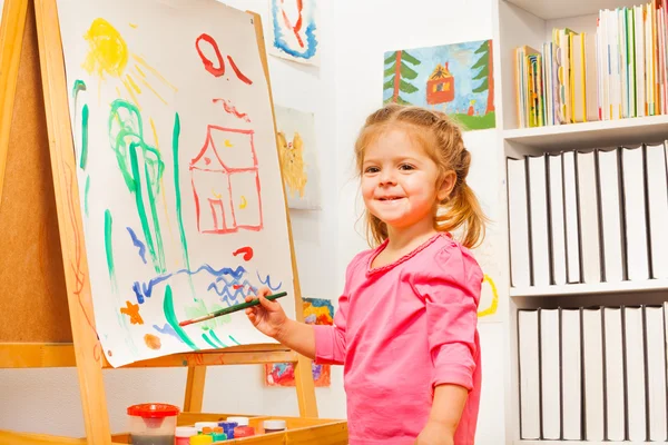 Menina bonito está desenhando usando um pincel no cavalete — Fotografia de Stock