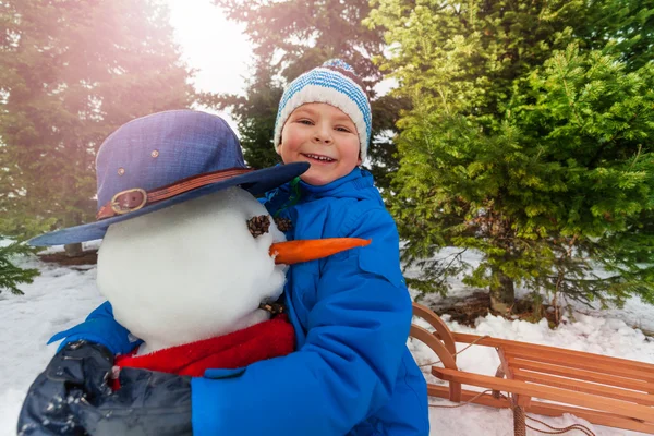 Gelukkig jongetje knuffels sneeuwpop — Stockfoto