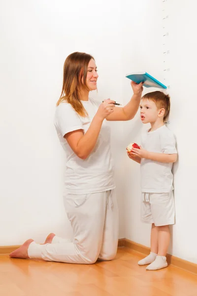 Mother measuring her son's height at the wall — Stock Photo, Image