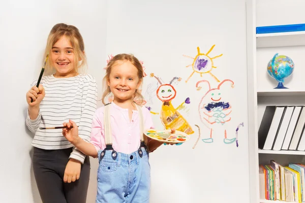 Two happy girls drawing funny picture at the wall — Stock Photo, Image