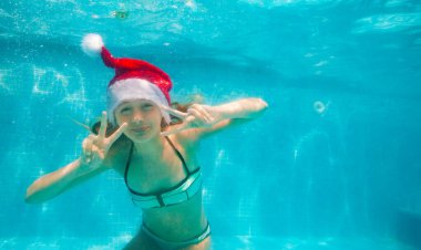 Mutlu kız havuzda dalıp yüzerken Noel Baba şapkası takıyor.