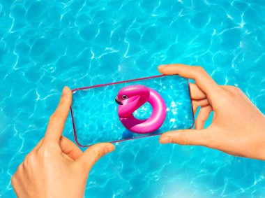 Yüzme havuzunda şişirilebilir flamingo şamandırasıyla fotoğraf çeken eller cep telefonunu tutuyor.