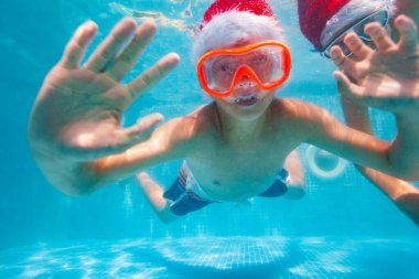 Mutlu çocuk havuzda dalıp yüzerken Noel Baba şapkası takıyor.