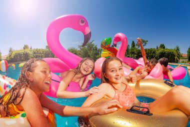 Birçok gülen kız yaz boyunca yüzme havuzunda bir grup arkadaş içinde şişme oyuncakla yüzer ve yüzer.