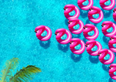 Şişme flamingo şamandıraları palmiye ağacının altından havuz manzarasında yüzerler.