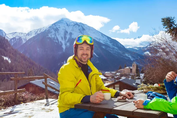 中午时分 戴着滑雪头盔的快乐微笑的男人在山景尽收眼底的咖啡馆喝茶 — 图库照片