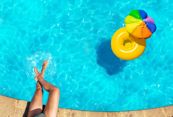 边界上的女人的腿和充气黄色的遮阳伞浮标在游泳池里游来游去 — 图库照片
