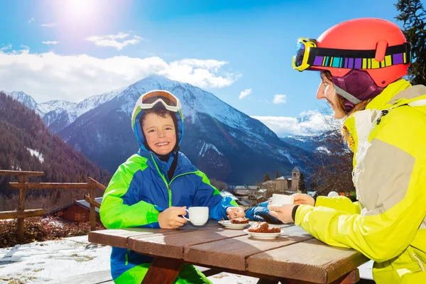 穿着滑雪服的小男孩和妈妈一起在山上的咖啡馆喝茶 — 图库照片