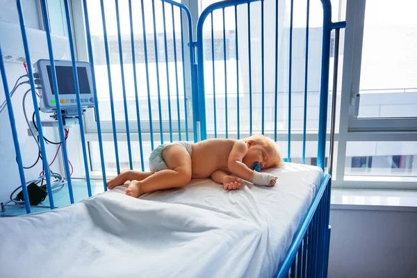 小さな1歳の幼児は 手とペースメーカーでカテーテルを操作した後 病院で寝る — ストック写真