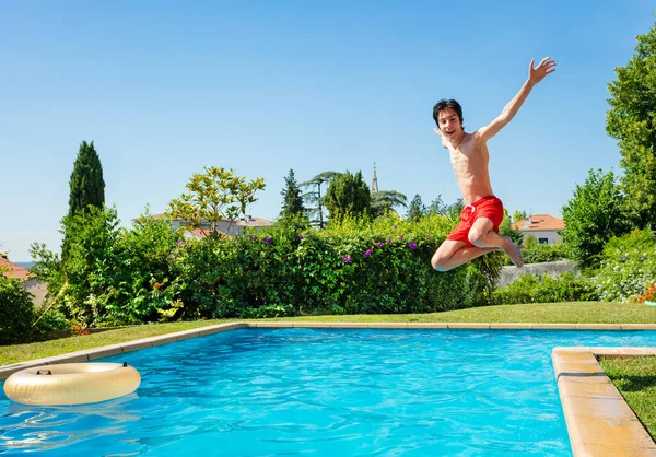 소년이 공중으로 뛰어올라 옆에서 비명을 지르고 웃으며 수영장 속으로 뛰어들다 — 스톡 사진
