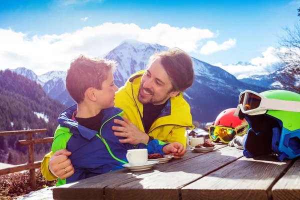 父亲穿着滑雪服 面带微笑地拥抱着小男孩 享受着滑雪场上的午休 — 图库照片