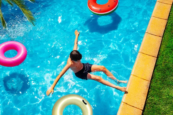 男孩跌在水里伸出手跳进游泳池 上面有许多甜甜圈和充气玩具 — 图库照片
