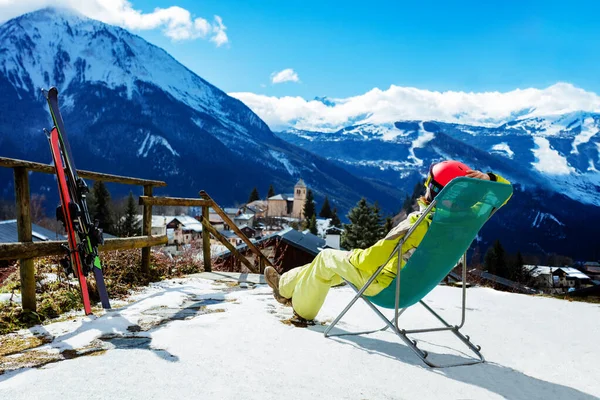 年轻女子在靠近一对滑雪板的甲板椅子上休息 观察高山和高山 — 图库照片