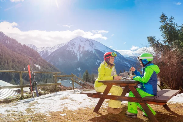 妈妈穿着滑雪服和年轻快乐的男孩坐在一起 滑雪后享受高山美景的午休 — 图库照片