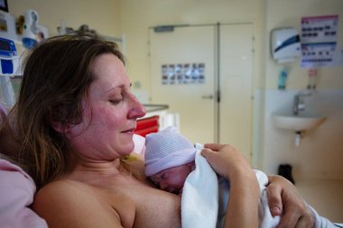 Yorgun kadın hastane yatağında doğum yaptıktan sonra yeni doğan bebeği kucağına aldı.