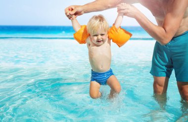Babam yüzme havuzunda bebekle oynuyor. Şişme omuz kemeri takıyor.