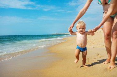 Yakışıklı küçük çocuk yaz tatilinde elini kolunu sallayarak deniz kenarında yürüyor.