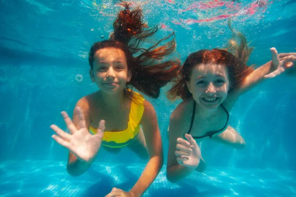 Dwie Szczęśliwe Dziewczyny Pływają Pod Wodą Machają Ręką Kamery Uśmiechając — Zdjęcie stockowe