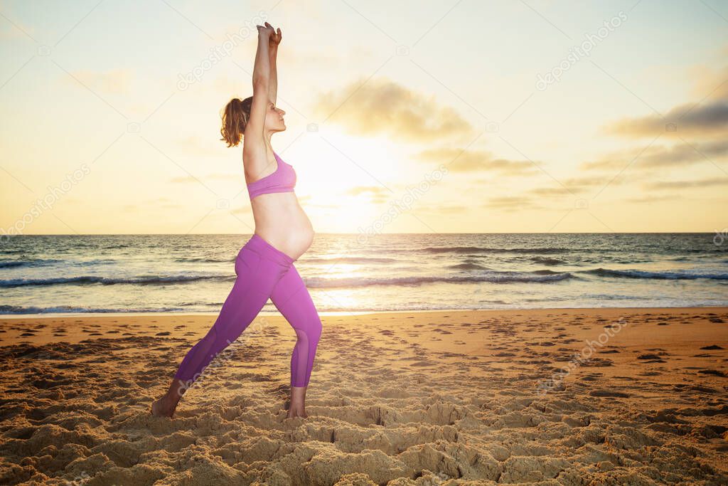 Pregnant woman exercise sit down and stretch profile view on the sand ocean beach with sunset over water on background