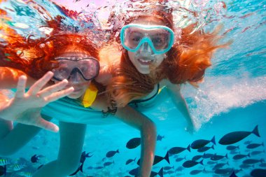 Dalgıç maskeli iki güzel kız suyun altında yüzer ve havuzda gülümseyen kameraya el sallar.