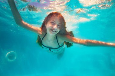 Güzel güler yüzlü mutlu bir kız portresi havuzda suyun altında yüzer.