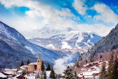 Panorama of Champagny-en-Vanoise village with mist and clouds around old church, over Courchevel resort on background clipart