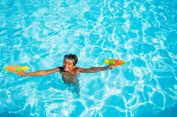 かわいいです10歳の男の子は水 ピストルで遊んでプールの水の中に立つ — ストック写真