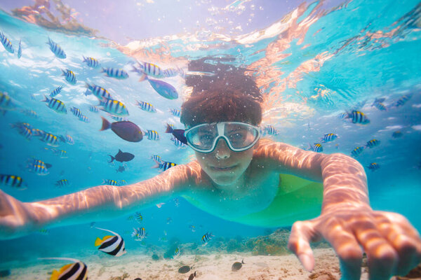 Portrait of the boy in scuba mask dive with fishes in the ocean looking at camera