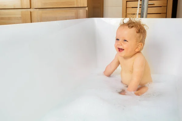 Happy portrait of a little toddler blond boy play in the bath with soap wide open mouth