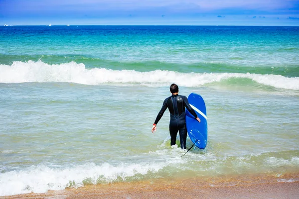 海の波にウェットスーツでサーフボードと歩いて男の後ろから肖像画 — ストック写真