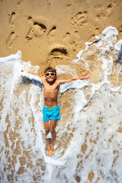 Θαλασσινά Κύματα Αγγίζουν Χαρούμενο Χαλαρό Αγόρι Ξαπλωμένο Στην Άμμο Τεντωμένα — Φωτογραφία Αρχείου