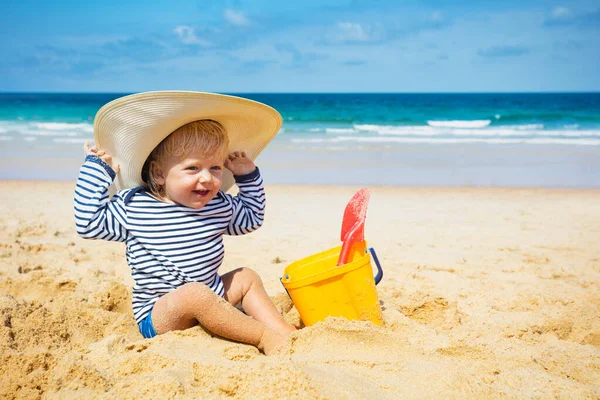 Szczęśliwy Mały Chłopiec Siedzieć Plaży Nosić Duży Słomkowy Kapelusz Grać — Zdjęcie stockowe