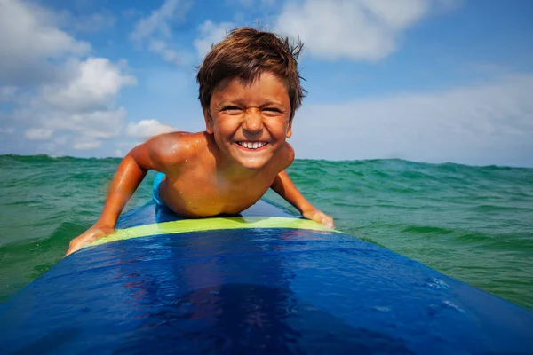 Close portrait of the boy on the surfing board smiling to the camera with funny head