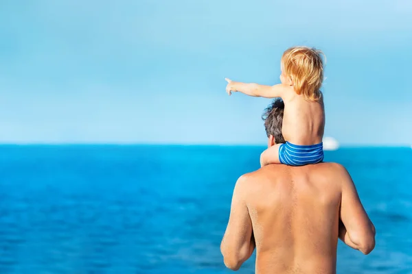 Mały Chłopczyk Siedzi Ramionach Ojca Wskazuje Morze — Zdjęcie stockowe