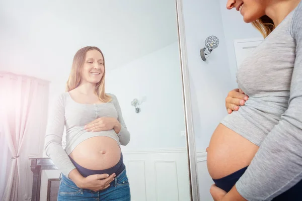 妊娠9ヶ月で窓の近くにポーズ腹と笑顔に触れる — ストック写真