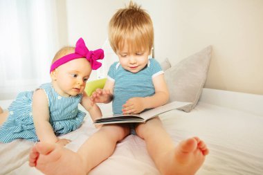 Baby boy read book to little infant girl sitting together in the bed