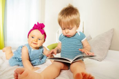 Little baby kids look and read book smiling together in the bedroom