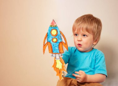 Toddler boy play astronaut holding paper rockets and planets at home with expression making sound of liftoff