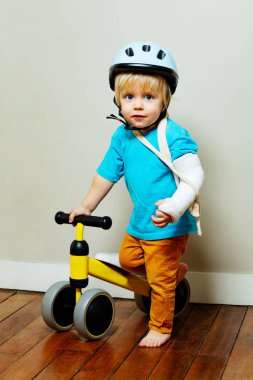 Portrait of the boy with broken hand in plaster holding kids bike standing by the wall
