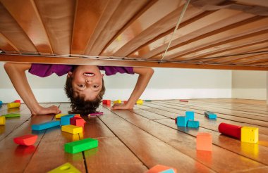 Boy look down under the bed stand on hands floor full of toy blocks